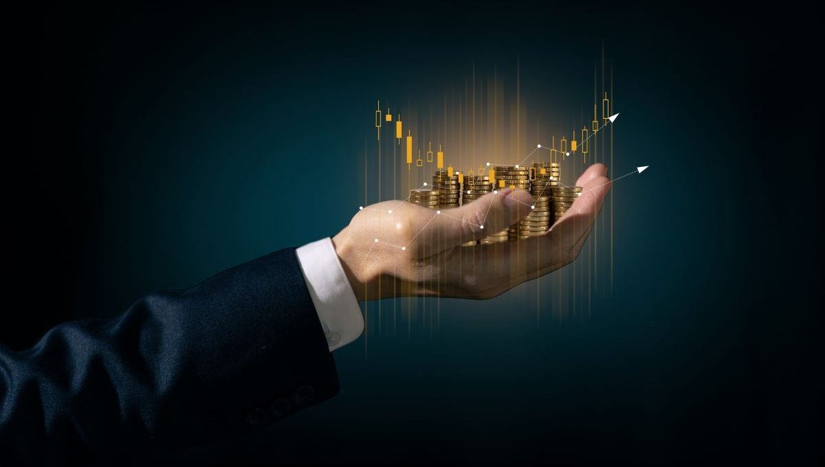 Imagem de uma mão segurando moedas de ouro e gráficos financeiros ascendentes, simbolizando gestão patrimonial, crescimento financeiro e investimentos, ideal para conteúdo de finanças e economia.